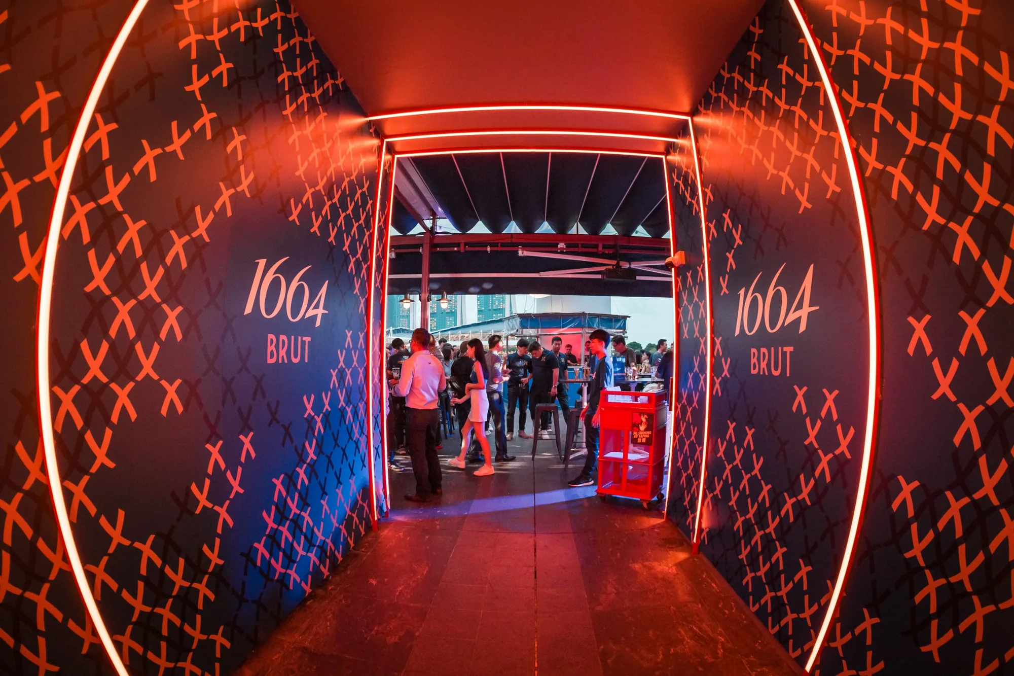 The entrance tunnel, lit in red and lined with the 1664 Brut cross pattern, opening onto the rooftop