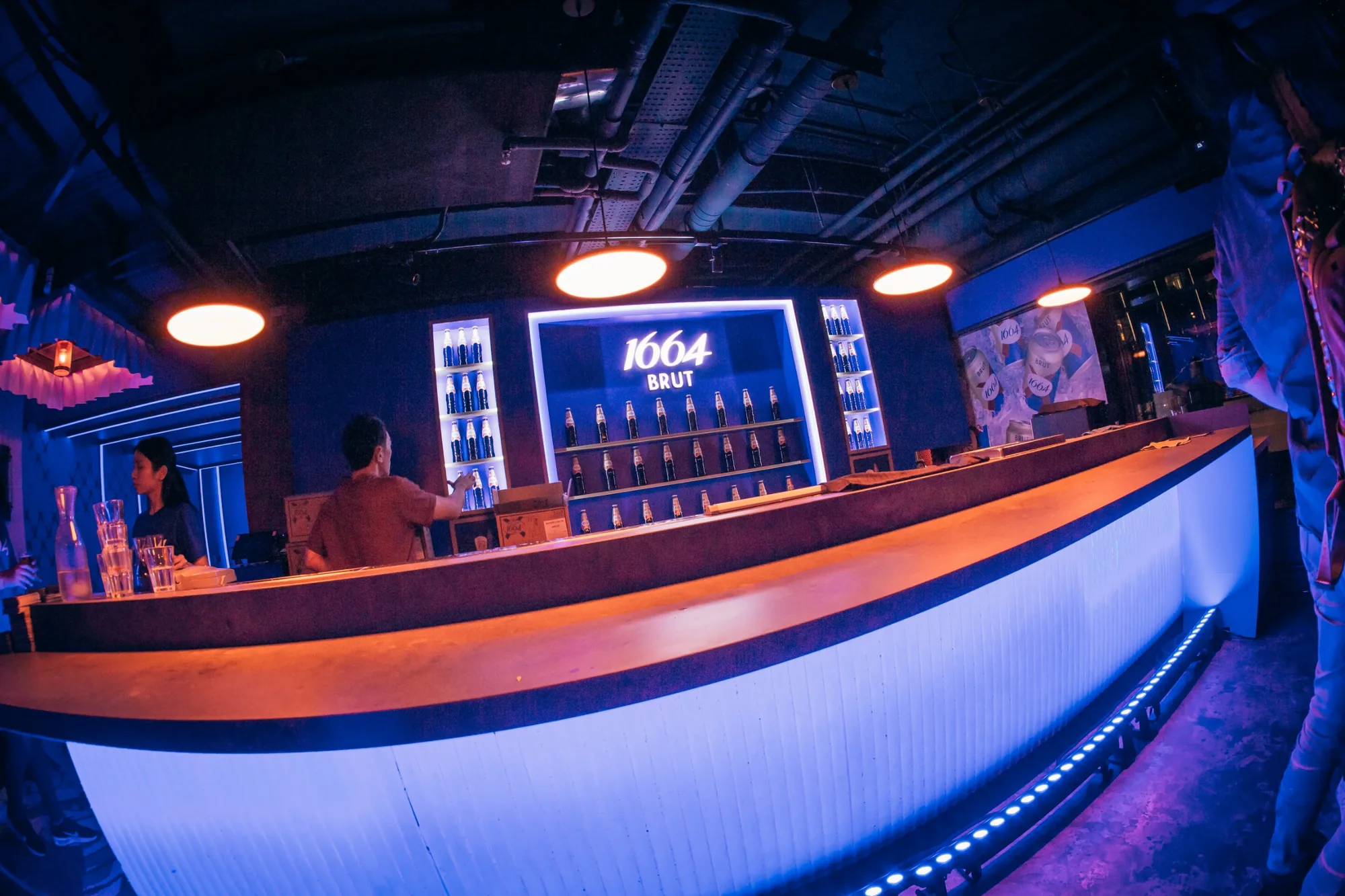 The curved bar under copper pendants, with the lit 1664 Brut back bar