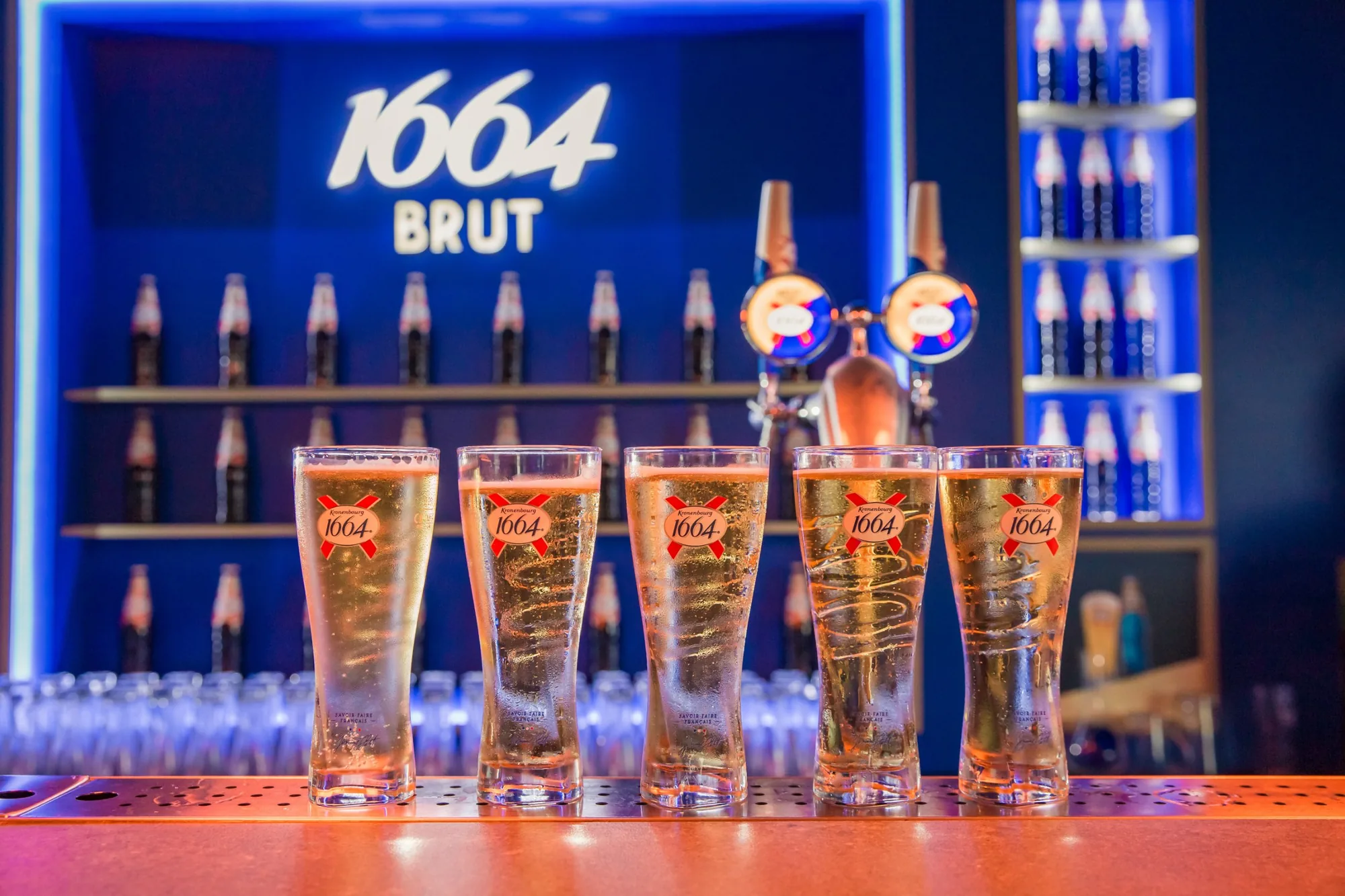 Five glasses of 1664 on the bar in front of the back bar
