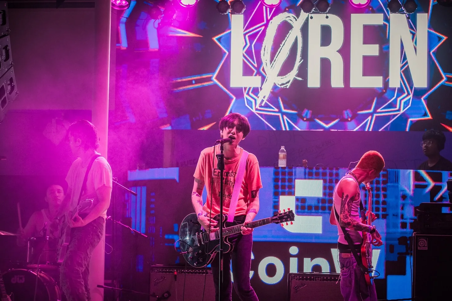 A band performing in front of the LØREN and CoinW screens