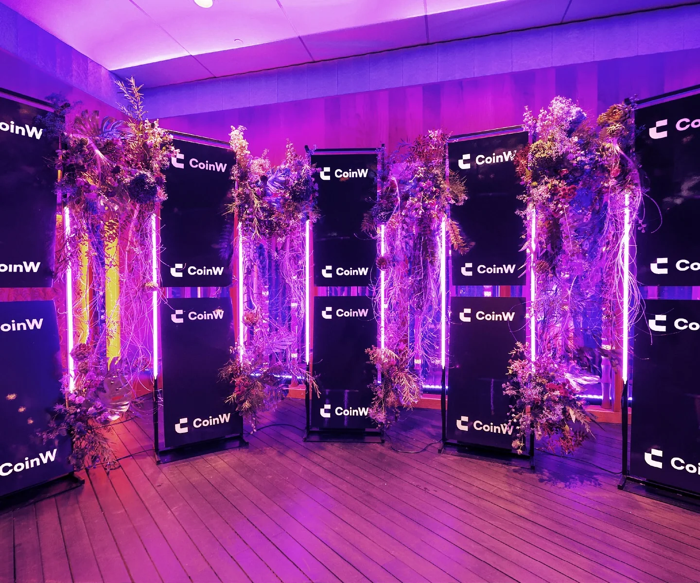 Floral installations framing CoinW panels under purple light