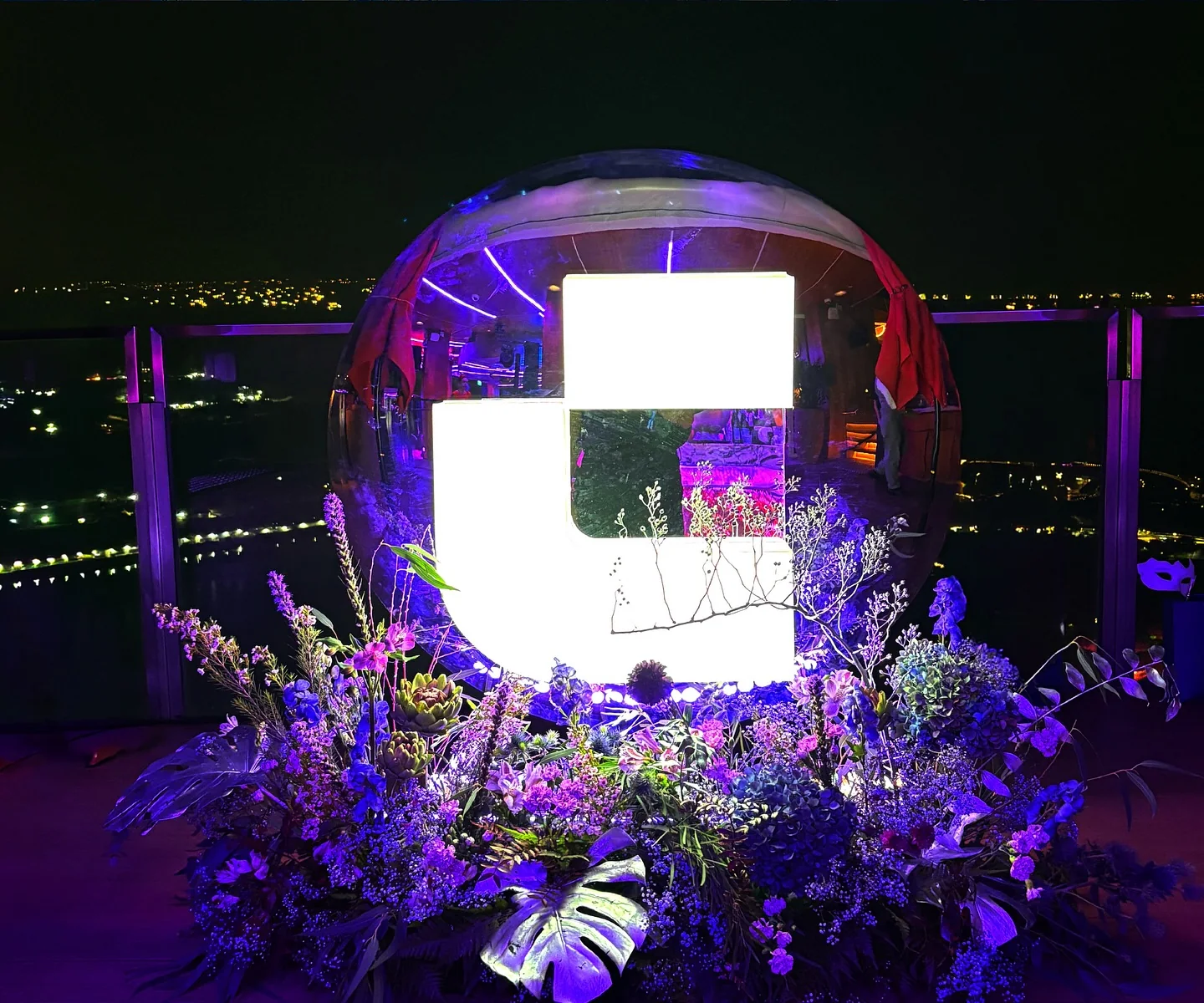 A glowing CoinW logo sphere set in flowers on the rooftop